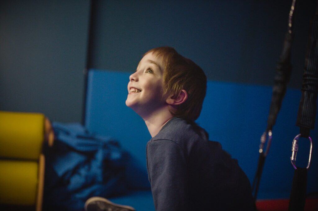 Young boy smiling up at a screen in a dimly lit room