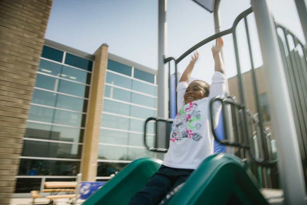 Young girl smiling going down a slide in an outdoor park
