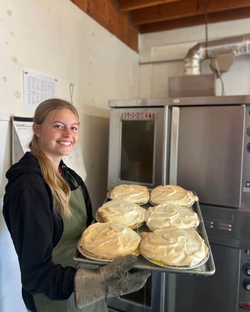 Staff member smiling with a tray of pies in the kitchen
