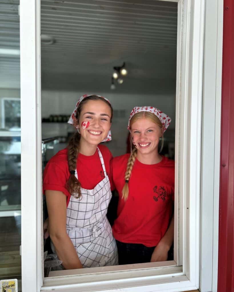 Two staff dressed up for Canada Day and smiling through the delivery window